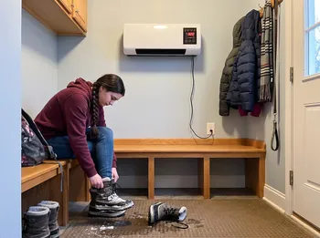 Teen pulling off snow boots in the mudroom under Power Heat Pro
